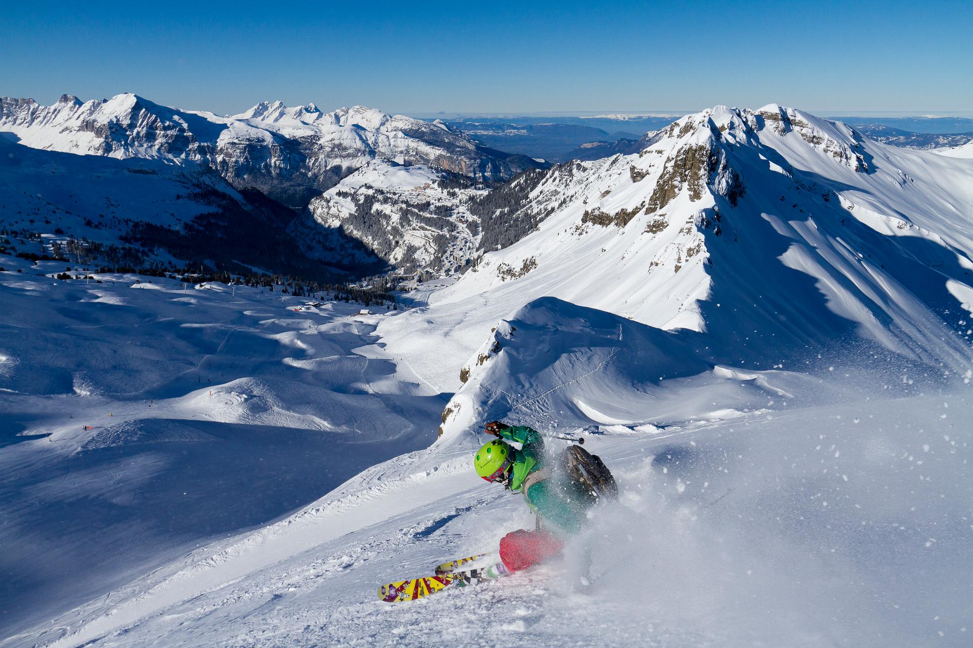 Skiier carving turn down ski slope with French Alps in background
